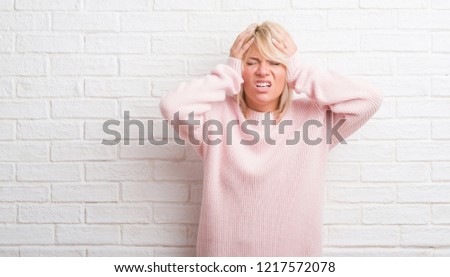 Adult caucasian woman over white brick wall wearing winter sweater suffering from headache desperate and stressed because pain and migraine. Hands on head.