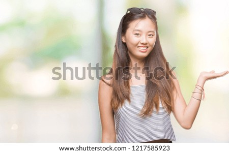 Young asian woman wearing sunglasses over isolated background smiling cheerful presenting and pointing with palm of hand looking at the camera.
