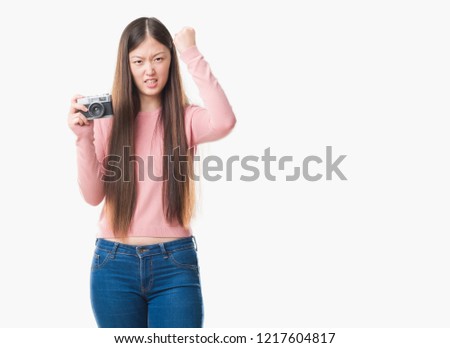 Young Chinese woman over isolated background taking pictures using vintage camera annoyed and frustrated shouting with anger, crazy and yelling with raised hand, anger concept
