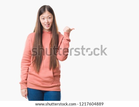 Young Chinese woman over isolated background wearing sport sweathshirt smiling with happy face looking and pointing to the side with thumb up.