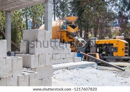 Photo of a construction with the bricks piled up in the foreground and in the background a concrete truck working
