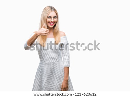 Young beautiful blonde woman wearing glasses over isolated background doing happy thumbs up gesture with hand. Approving expression looking at the camera with showing success.