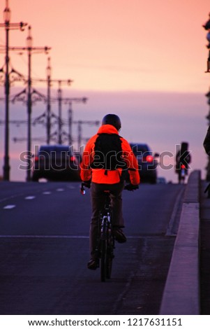 cyclist in an orange jacket with a backpack on a bridge at sunset