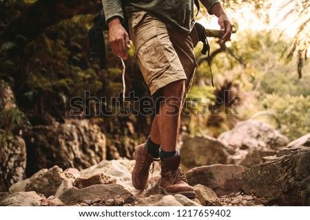 Low section of man in trekking gear walking through rocky trail. Man hiking through rocky mountain trail. Royalty-Free Stock Photo #1217659402