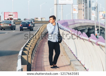 The guy is standing near the road on the bridge