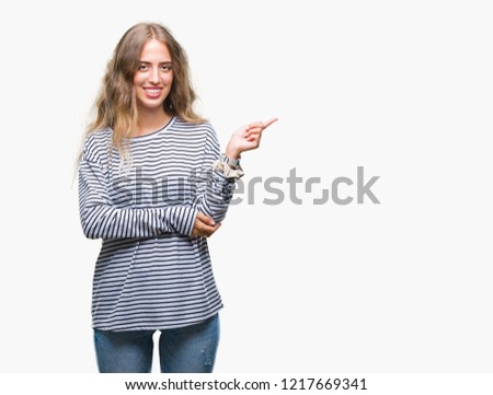 Beautiful young blonde woman wearing stripes sweater over isolated background with a big smile on face, pointing with hand and finger to the side looking at the camera.