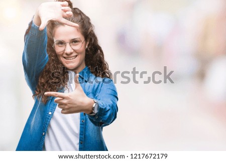 Beautiful young brunette curly hair girl wearing glasses over isolated background smiling making frame with hands and fingers with happy face. Creativity and photography concept.