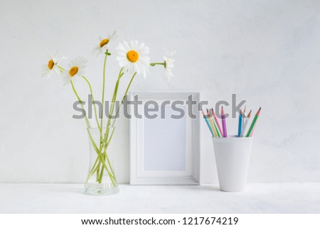 Home interior with decor elements. White frame, flowers in a vase, pencils