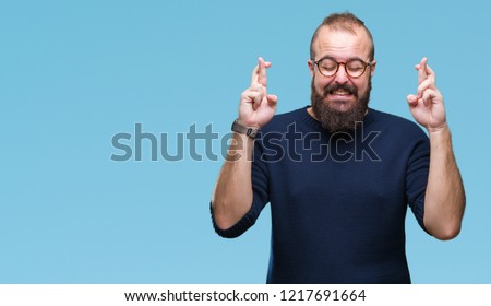 Young caucasian hipster man wearing sunglasses over isolated background smiling crossing fingers with hope and eyes closed. Luck and superstitious concept.