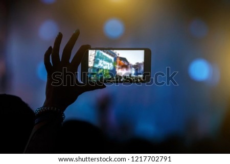 Hand with a smartphone records live music festival and taking photo of concert stage.