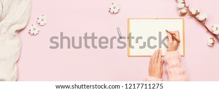 Female hands in pink knitted sweater written with a pen in open clean notebook and cotton on pink pastel table top view flat lay Fashion blogger working desk Cotton flowers Lifestyle gentle background