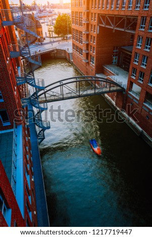 Small Boat under bridge over canal between red brick buildings in the old warehouse district Speicherstadt in Hamburg in golden hour sunset light, Germany. View from above