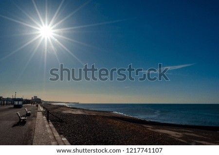 Brilliant sunlight with lens flare over a silhouetted beach and promenade at Brighton and Hove