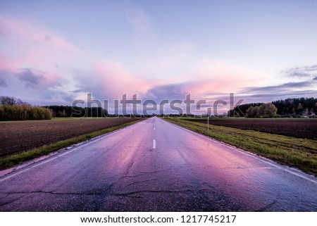 Colorful sunset clouds over the country asphalt road, fields and forests. Latvia
