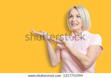 Happy middle aged woman pointing at copyspace isolated on yellow background