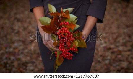 The girl is holding a bouquet of lingonberries and autumn yellow leaves against the background of autumn forest and fallen leaves. Autumn picture. Golden autumn