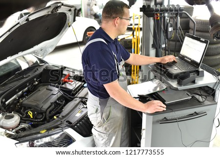 car mechanic maintains a vehicle with the help of a diagnostic computer - modern technology in the car repair shop Royalty-Free Stock Photo #1217773555