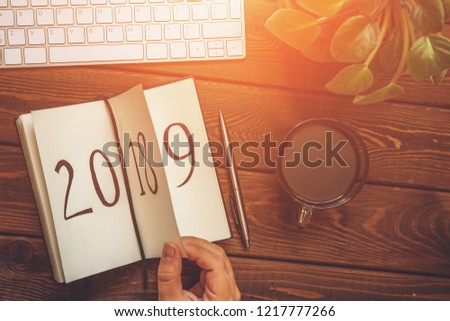Top view of female hand flips notepad sheet on wooden table. 2018 is turning, 2019 is opening, toned with light effect Royalty-Free Stock Photo #1217777266