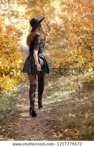 beautiful woman in black dress and hat walking on a background of yellow autumn leaves