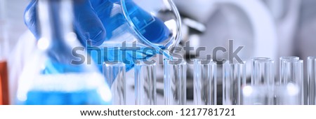 A male chemist holds test tube of glass in his hand overflows a liquid solution of potassium permanganate conducts an analysis reaction takes various versions of reagents using chemical manufacturing. Royalty-Free Stock Photo #1217781721