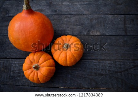 Three orange pumpkins laying on a wooden table. Two kinds.