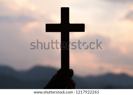 Woman hand holding holy lift of christian cross with light sunset background. Royalty-Free Stock Photo #1217922265