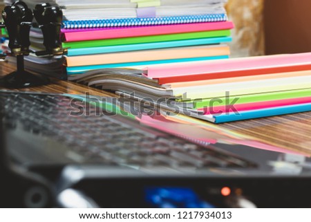 Pile of unfinished documents on office desk. Stack of homework assignments archive with colorful plastic slide binder bars on teacher's table waiting to be managed. Education and business concept.