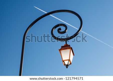 Shining Backlit Streetlamp and Airplane Trail in Background, Megeve, France