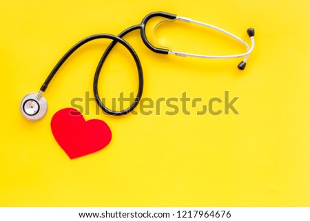 Health care concept. Stethoscope near heart sign on yellow top view copy space