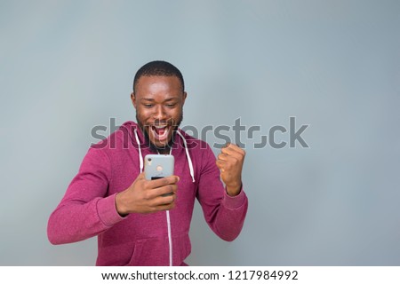 young black man excited and celebrating while holding and looking at his phone  Royalty-Free Stock Photo #1217984992