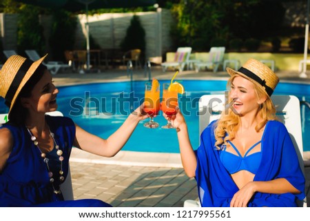 Happy cute young women with cocktails laughing and having fun near swimming pool