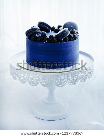 Beautiful dark blue cake with macarons, fresh blackberry ans blueberry