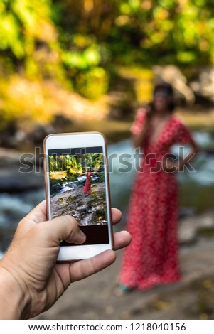 Man taking photo of woman in long red dress in nature of Bali island.
