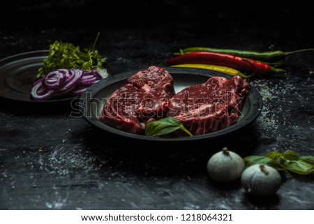 on a dark background fresh, red, raw beef and spilled coarse salt, next to it lies fresh, colorful vegetables and herbs