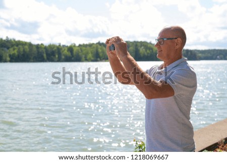 Happy Senior Man Taking Picture With Phone By The Lake