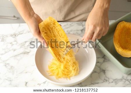 Woman scraping flesh of cooked spaghetti squash with fork in kitchen Royalty-Free Stock Photo #1218137752