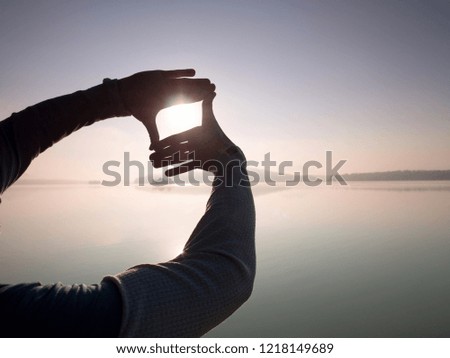 Fingers gesturing picture frame on sunrise seaside. Sunlight on beach. Sunset at the sea. Hand-made gesture in love concept.