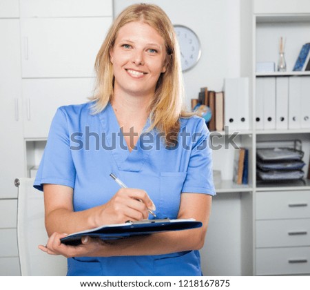 Smiling female nurse in formal wear registering information in form