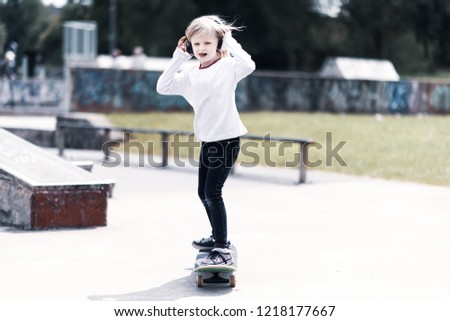 A pretty little girl with blonde hair at the local skateboard park practicing and riding around