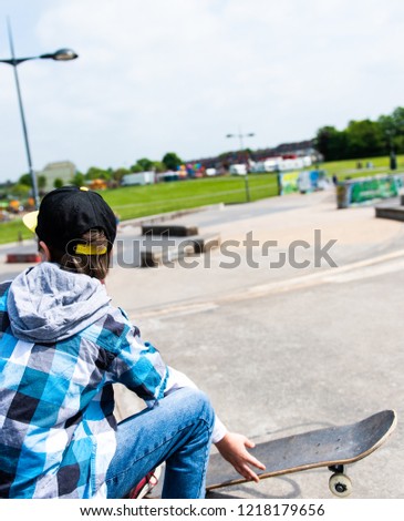 A little boy with ADHD, Autism, Aspergers Syndrome, enjoys a day at the skatepark, listening to music and skateboarding, wearing a baseball cap and shirt