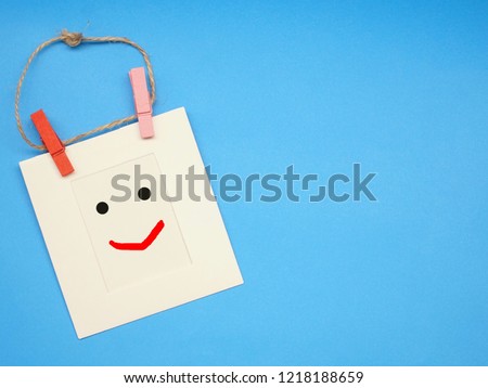 Top view of white frame paper with hand writing emotion "smile face" and wood clip on blue table. Feel happy and funny. Free space for any text design.