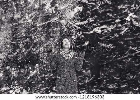 Stylish cheerful girl in a sweater in the winter forest. Snow from tree falls on the girl