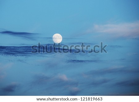 Full moon over blue evening sky with thin clouds