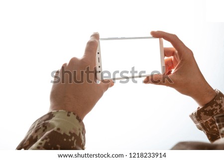 US Army. Young soldier holding a mobile phone with blank screen on white background