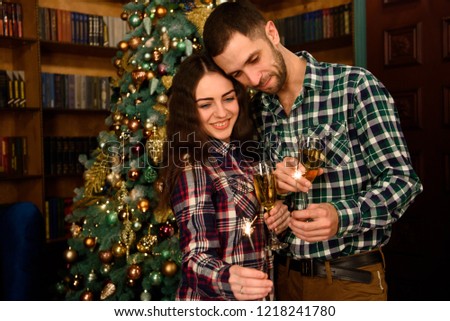 Merry Christmas and Happy New Year! Attractive young couple is celebrating holiday at home together, drinking champagne and smiling with Bengal lights in hand