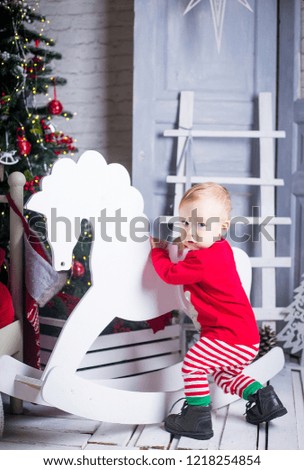 cute baby in a red sweater and striped tights is played next to the Christmas tree