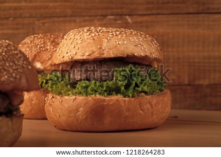 Big tasty appetizing fresh burgers of green lettuce red tomato cheese and bacon slice meat cutlet and white bread bun with sesame seeds closeup, horizontal picture