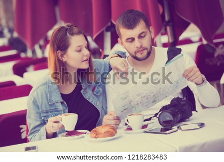 Young man and woman sitting with coffee and looking at map in cafe