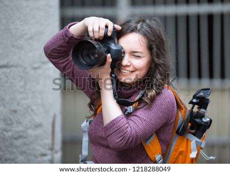 smiling girl photographer holding camera in hands and photographing in city
