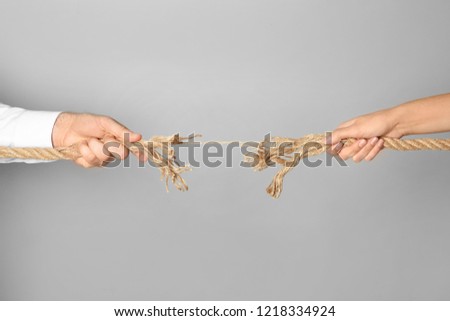 Man and woman pulling frayed rope at breaking point on gray background Royalty-Free Stock Photo #1218334924